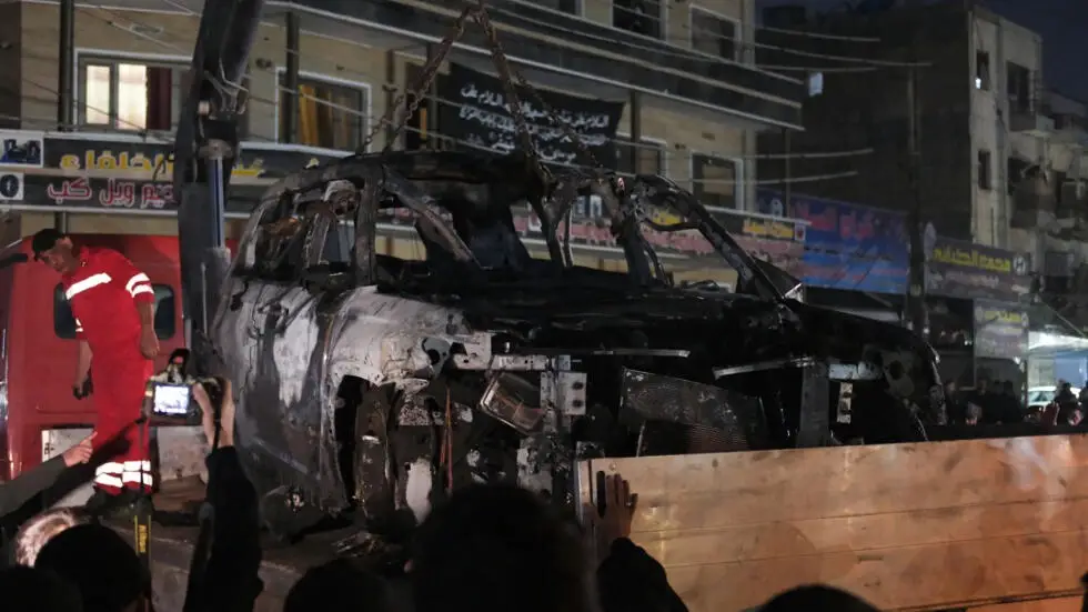 People watch as a vehicle that was hit by a deadly drone strike is removed from a Baghdad neighbourhood