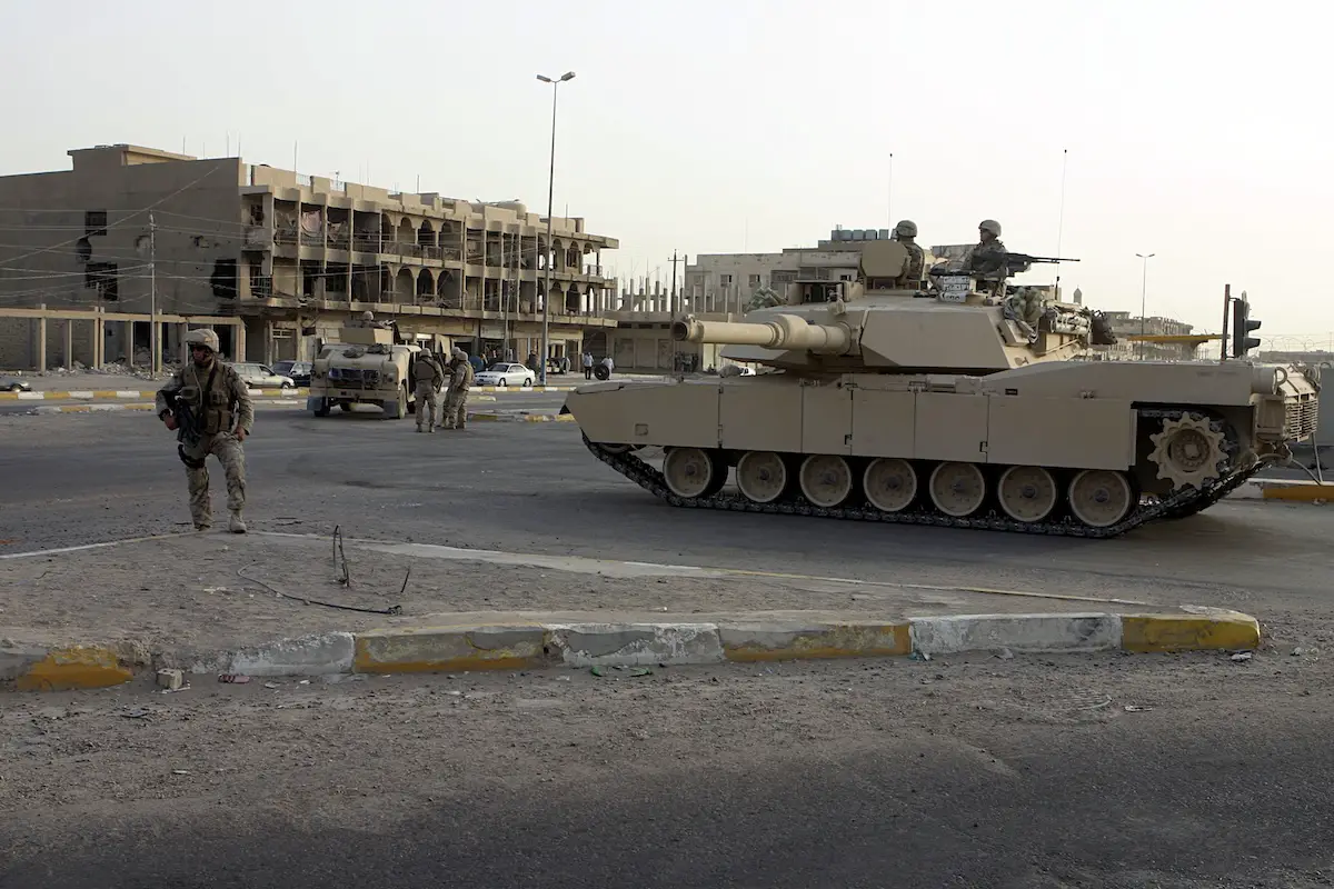 An M1A1 Abrams tank provides area security alongside a street intersection beside Marines during a 2005 operation in Fallujah, Iraq
