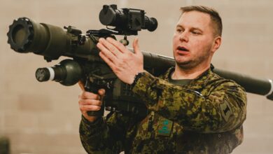 A soldier wearing a camouflaged uniform appears to be demonstrating how to carry the Piorun portable missile launching system. He has the equipment resting on his right shoulder, pointing it to the upper left side of the image.