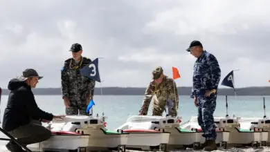 (From Left) Michael Novitzky, Warrant Officer Richard Comfort, Lieutenant Colonel Charles O'Donnell and Squadron Leader Robert Morris discuss the SWARMS Sea Robotics unmanned vehicles capability during the Technical Cooperation Program AI Strategic Challenge 2023 at HMAS Creswell, Jervis Bay Territory. *** Local Caption *** The Technical Cooperation Program (TTCP) AI Strategic Challenge (AISC) 2023 will be held at HMAS Creswell, 09-27 October 2023. Bringing together Five Eyes (FVEY) nations personnel, AISC 2023 will have a program of live experiments and demonstrations across a variety of systems, situated in a scenario representative of a full military operation. AISC 2023 is seeking to accelerate the transition of Artificial Intelligence (AI) solutions into the hands of coalition armed forces.