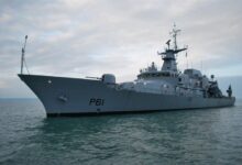 An Irish Naval Service's offshore patrol vehicle, LÉ Samuel Beckett (P61), is seen sailing calm, green-blue waters. The gray ship has "P61" painted on its hull in black. The sky in the background is cloudy and slightly overcast.