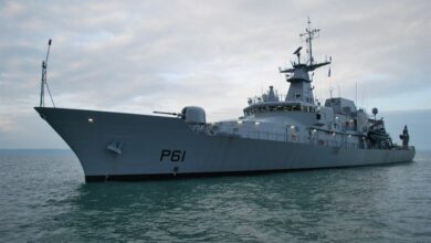 An Irish Naval Service's offshore patrol vehicle, LÉ Samuel Beckett (P61), is seen sailing calm, green-blue waters. The gray ship has "P61" painted on its hull in black. The sky in the background is cloudy and slightly overcast.