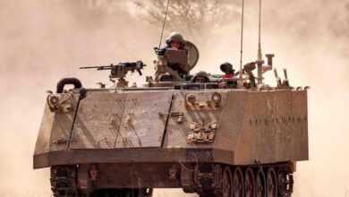 An Israeli army armored tracked vehicle moves near a stationed artillery howitzer at a position along the border with the Gaza Strip in southern Israel