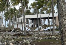 The Roi-Namur church steeple rests on the coral-strewn grounds on the opposite side of the Tradewinds Theater, background, from where it once stood