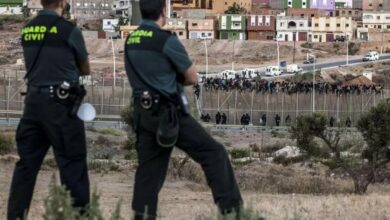 Spanish Guardia Civil watch as would-be immigrants from Africa sit atop a fence after scrambling over two other border barriers on Spain’s tiny north African territory of Melilla
