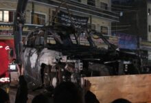 People watch as a vehicle that was hit by a deadly drone strike is removed from a Baghdad neighbourhood
