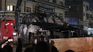 People watch as a vehicle that was hit by a deadly drone strike is removed from a Baghdad neighbourhood