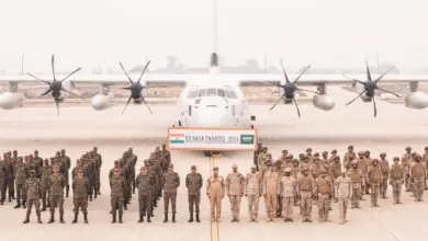 Uniformed soldiers from the Indian and Saudi Arabian Army stand in attention in front of a white plane in what appears to be an airport runway. Between the soldiers and the aircraft, a huge banner reads 'EX SADA TANSEEQ - 2024'. India's flag is on the leftmost side of the banner, while Saudi Arabia's is on the right. The background is a foggy gray sky with a barely visible skyline in the distance.