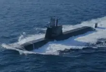 ROKS Dosan Ahn Changho (SS-083), a Jangbogo-III class submarine, is seen floating half-submerged in deep blue waters. The ship is painted black. A South Korean flag is seen hoisted up on a pole on top of the submarine's sail.