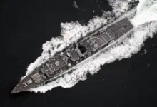 A UK Royal Navy ship is seen sailing deep dark-blue waters. The scene is shown from a top-down view.