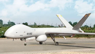 An Hermes 900 MALE drone is seen on the ground in what appears to be a runway. The white aircraft has 4X-USZ written on its left side in black paint.
